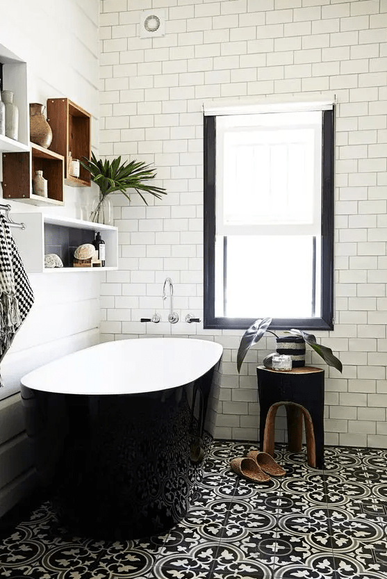 a chic, modern bathroom with black patterned and white subway tiles, a sleek black bathtub and box shelves, and a black stool