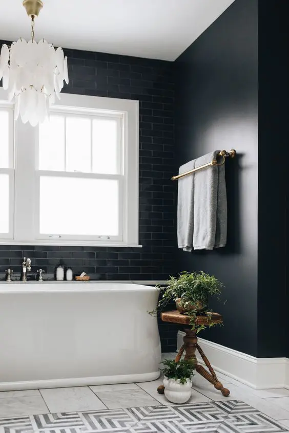 a beautiful and elegant bathroom with black walls and black tiles, a white bathtub, a black and white tile floor and a mother of pearl chandelier