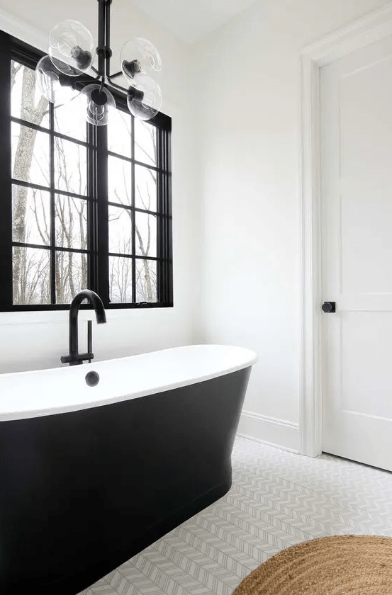 a black and white farmhouse bathroom with a black window frame, a sleek black tub, a cool chevron floor and a bubble lamp