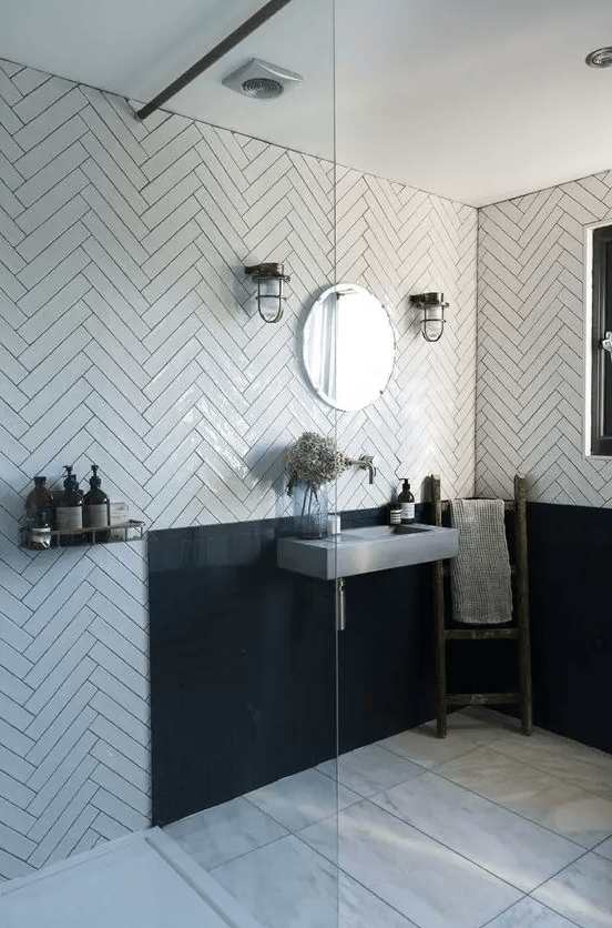 a striking and chic bathroom with white herringbone tiles, a black backsplash, a wall-mounted concrete sink and vintage lamps