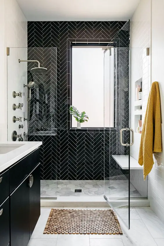 a black and white bathroom with herringbone tiles on the wall, a bench, niche shelves, a black vanity and a tile floor