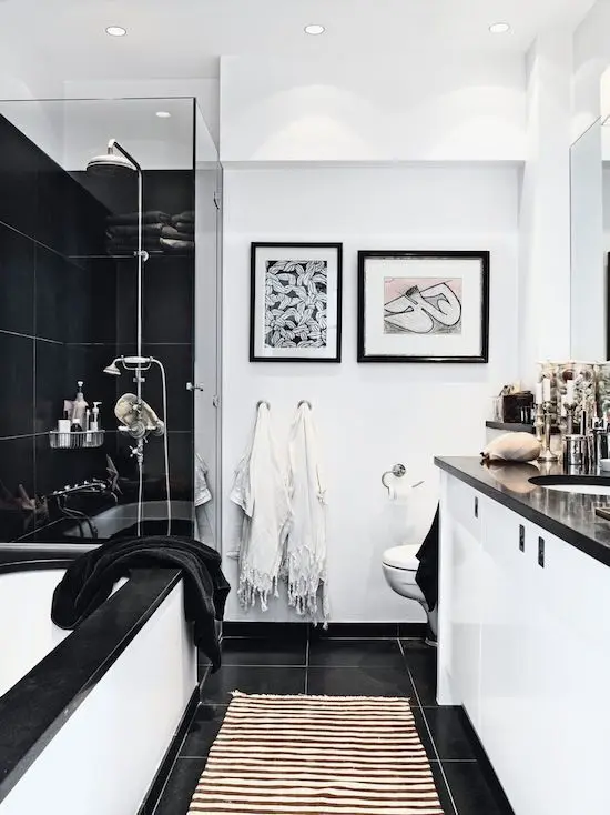a black and white bathroom with large format tiles, a black-rimmed bathtub, a black shower area and a white vanity