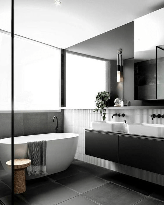a sophisticated Scandinavian bathroom with thin white and extensive black tiles, a black double vanity, an oversized mirror and a cork stool next to the bathtub