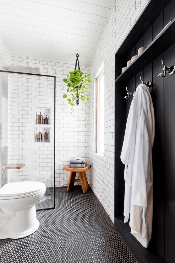 a Nordic bathroom with white subway and black penny tiles, a wood built-in, some greenery and niches in the shower area