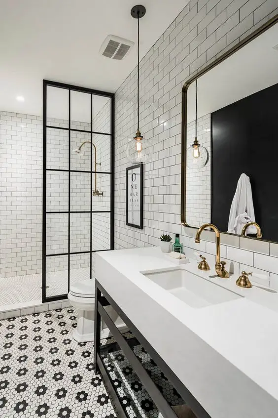 a sophisticated black and white bathroom with subway and penny tiles, a stand with sink, a large mirror and gold fixtures