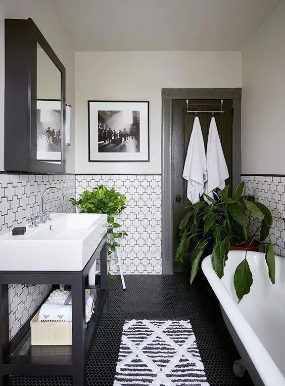 a pretty black and white bathroom with penny and eye-catching geometric tiles, a clawfoot tub, a sink on a black stand and a mirrored cabinet