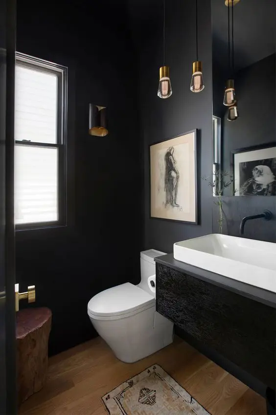 a small powder room with black walls, a black floating vanity, a mirror and hanging lamps, and a tree stump stool