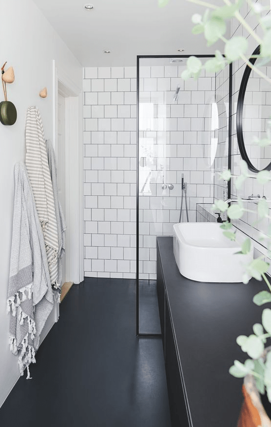 A Nordic bathroom with white square tiles, smooth black surfaces, black frame and a curved sink is very chic
