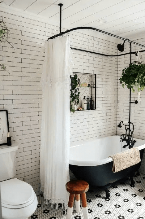A small retro bathroom with white subway and penny tiles, a black vintage bathtub, black fixtures and potted plants is cool