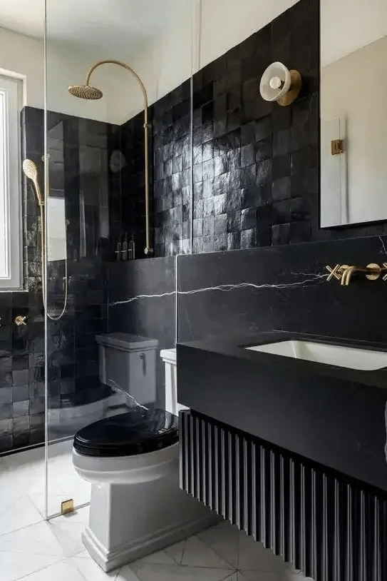 a modern, atmospheric bathroom with striking tiles and black marble, a floating vanity, gold fixtures and a mirror