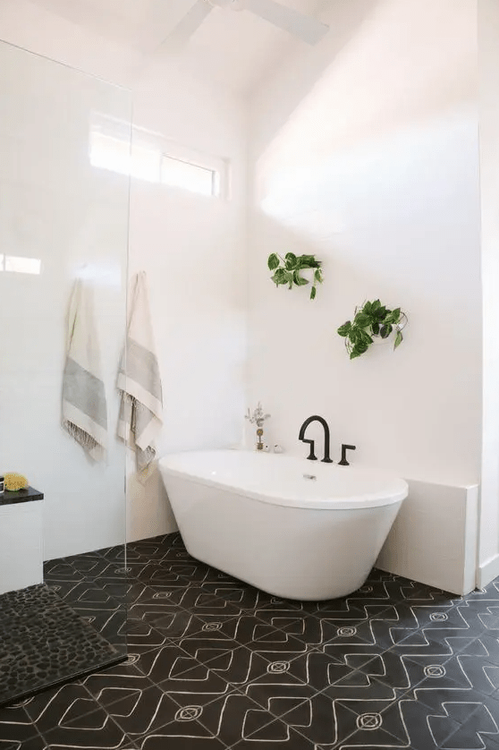 A stylish mid-century modern bathroom with white and black mosaic tiles, a bathtub, greenery and a black pebble rug