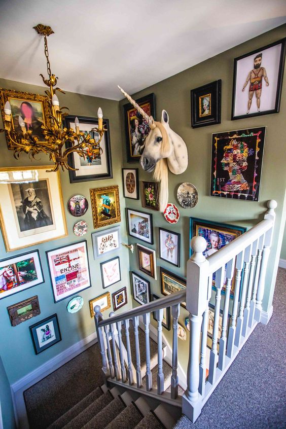 A super bold and fun maximalist gallery wall that takes up two walls and contains various artwork, plates and a unicorn head looks wow