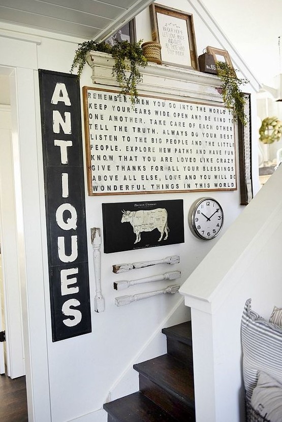 A rustic vintage gallery wall with signs in frames, railing pieces, green plants, ropes and some signs on the shelf