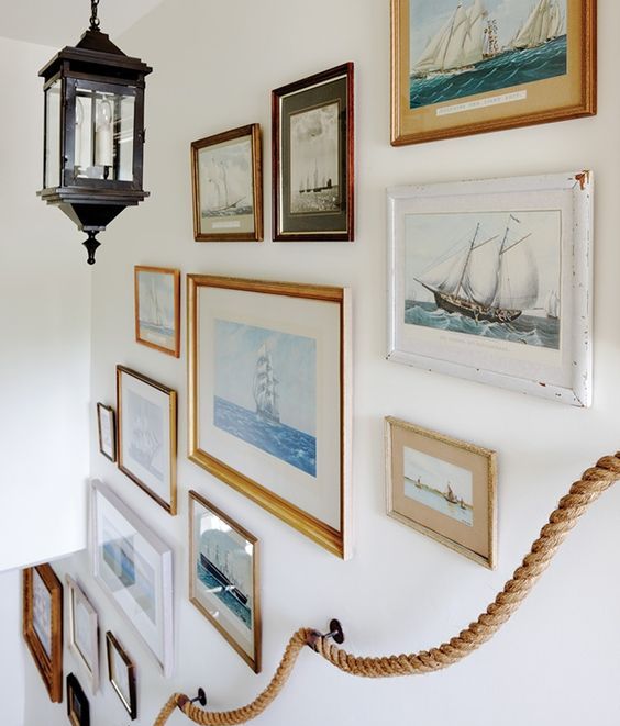 A coastal gallery wall with various seaside artwork and a rope railing is a beautiful idea for a seaside home