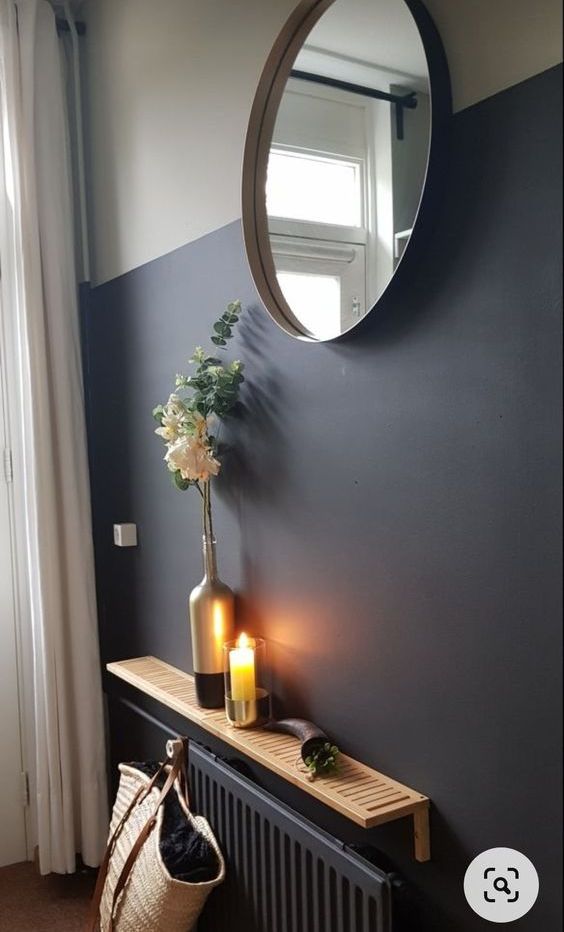a black radiator with a small, stained, fluted shelf with flowers, a candle and a round mirror above it