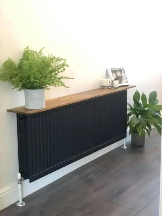 A black radiator with a stained shelf with potted plants, candles and some decor makes a very natural console table