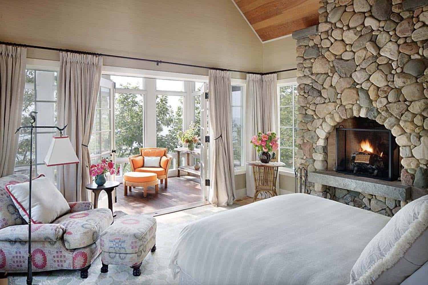 Lake house bedroom with stone-clad fireplace and sun-filled living room
