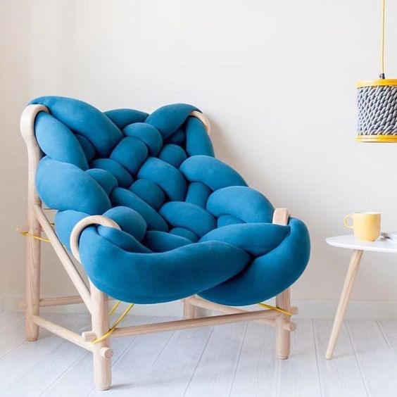 A super creative chair with a light stained wood frame and a piece of blue upholstery, all bent and wrapped to form a seat and backrest